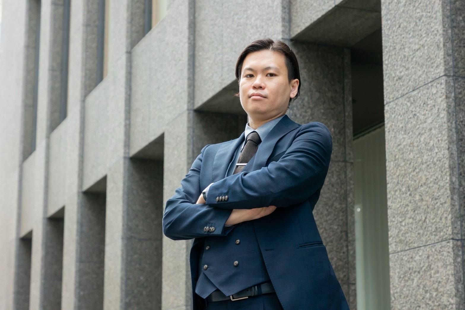 スーツ姿で腕を組み、まっすぐにカメラを見据えるBLAYN社員
